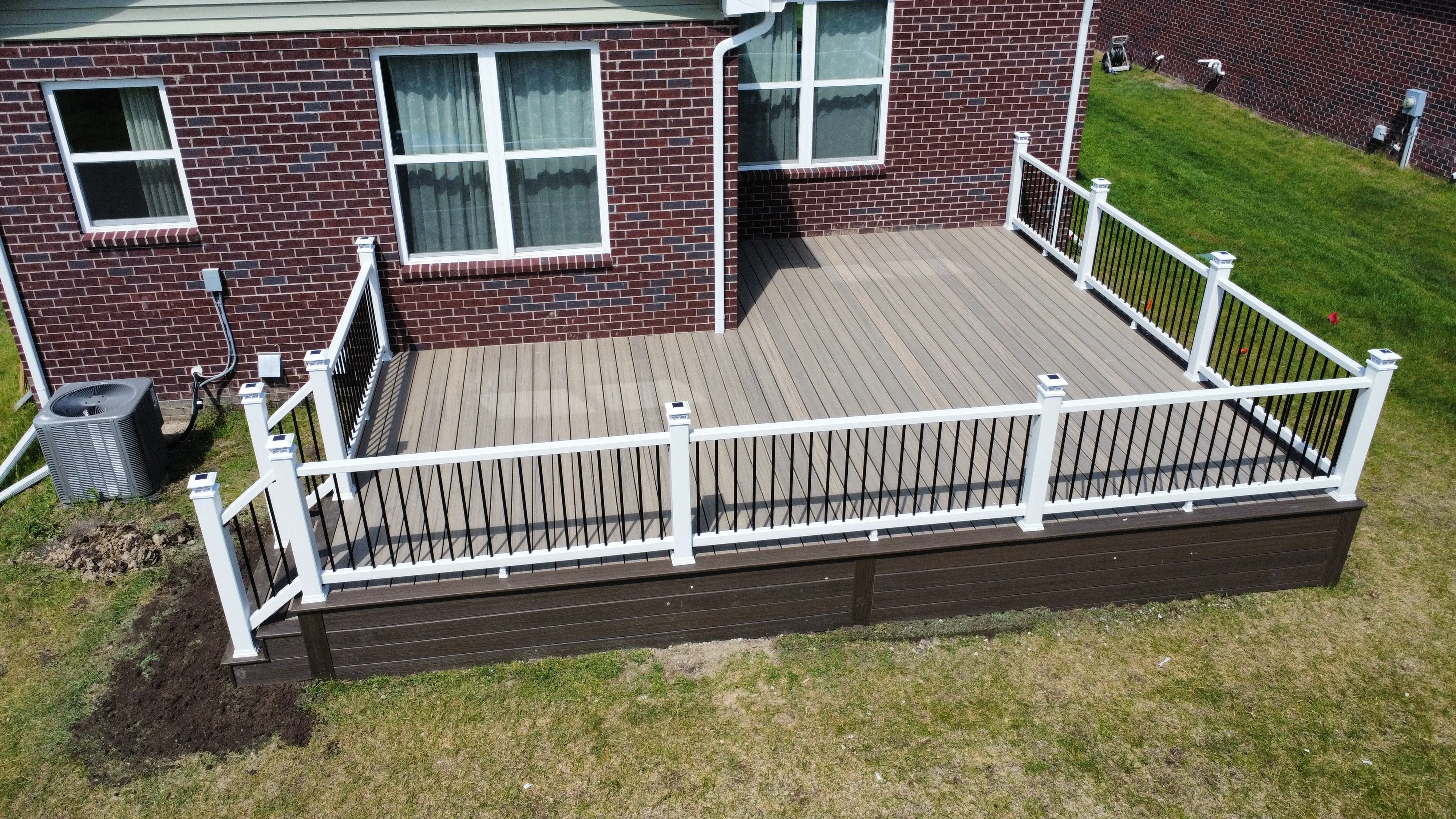 Elevated composite deck with white vinyl railings, black balusters, and brown decking boards