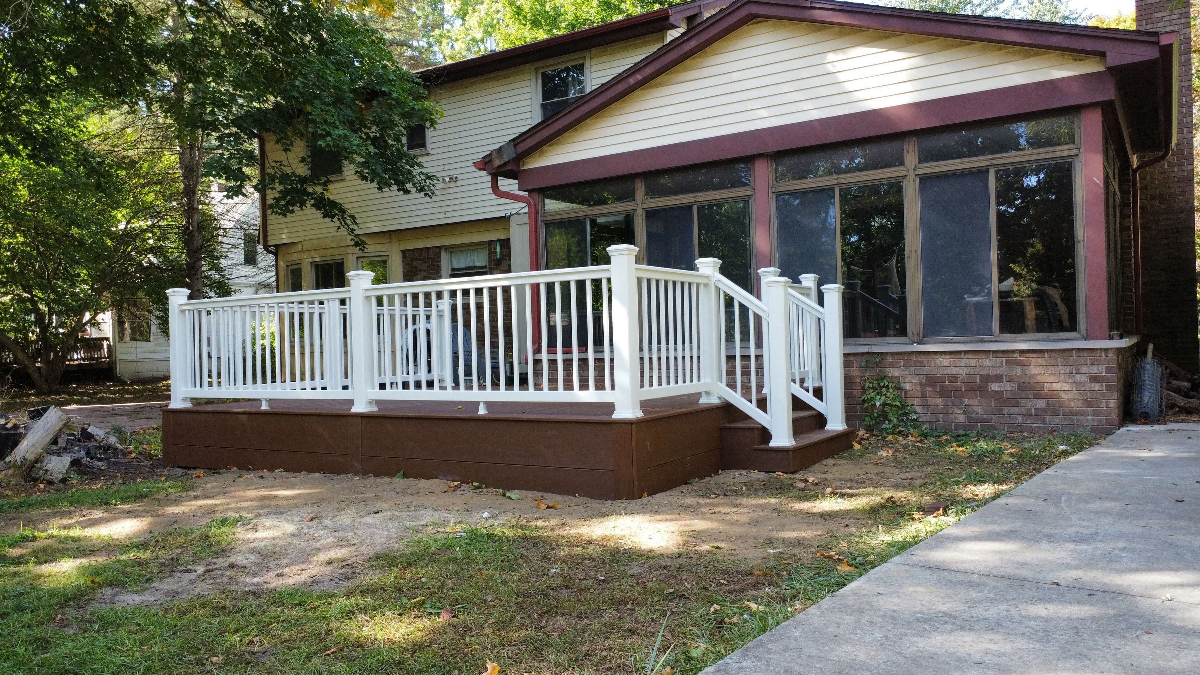 Elevated deck with white railings, brown fascia, and large sunroom addition with metal frame and windows