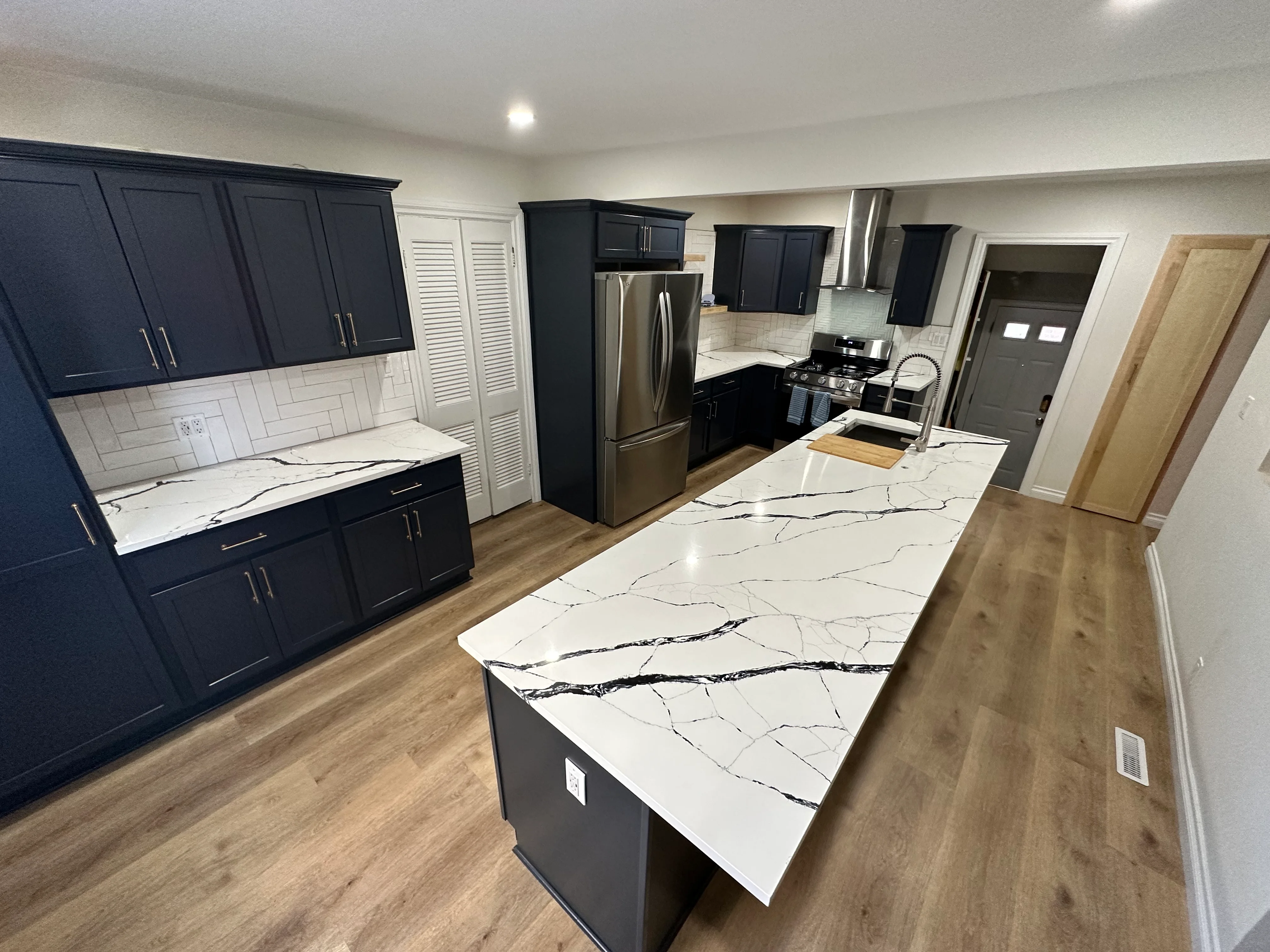 Dark navy kitchen cabinets, white quartz countertops with black veining, subway tile backsplash, stainless steel appliances
