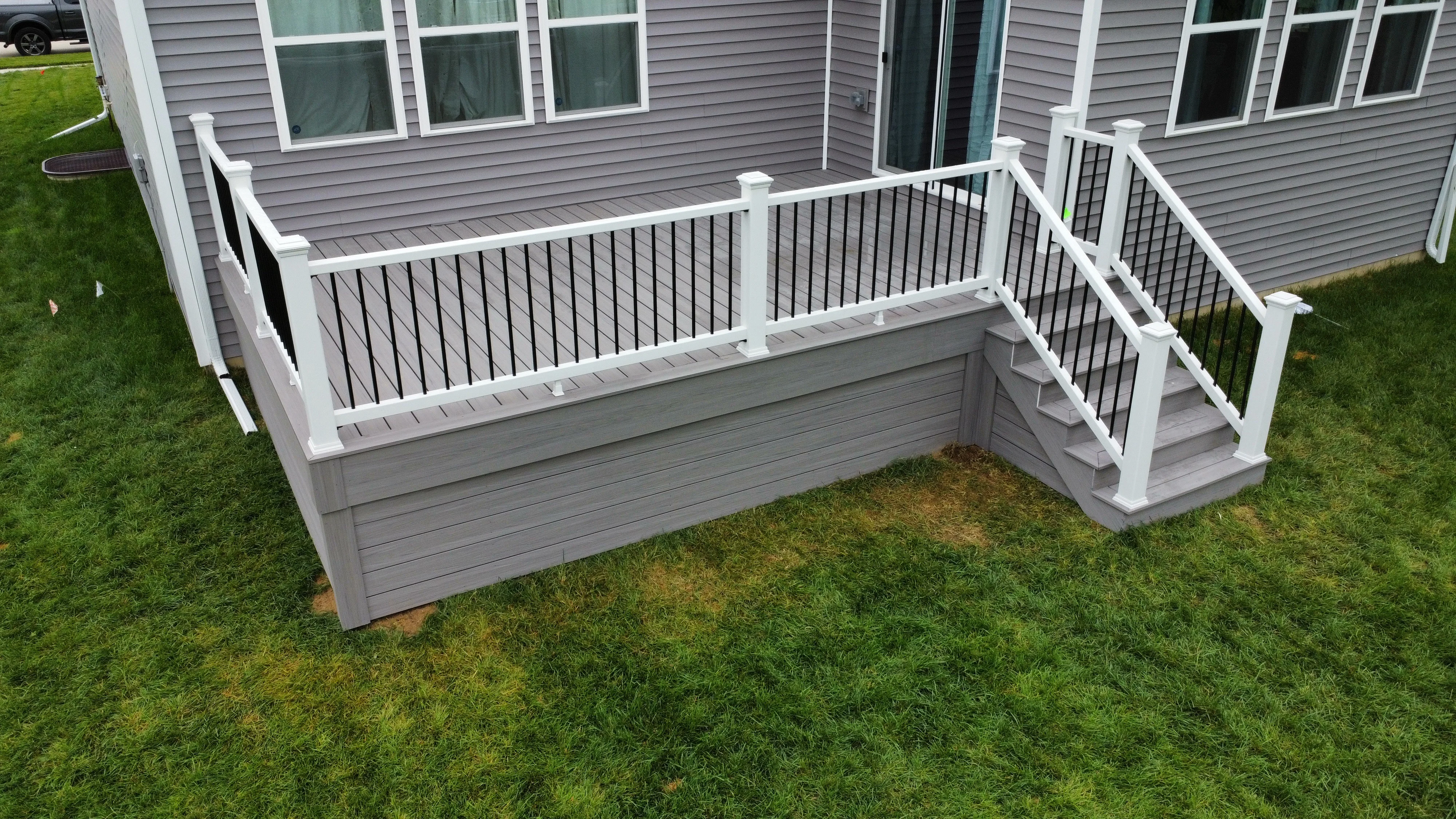 Two-tier composite deck with white railings, black balusters, and gray decking attached to gray siding home