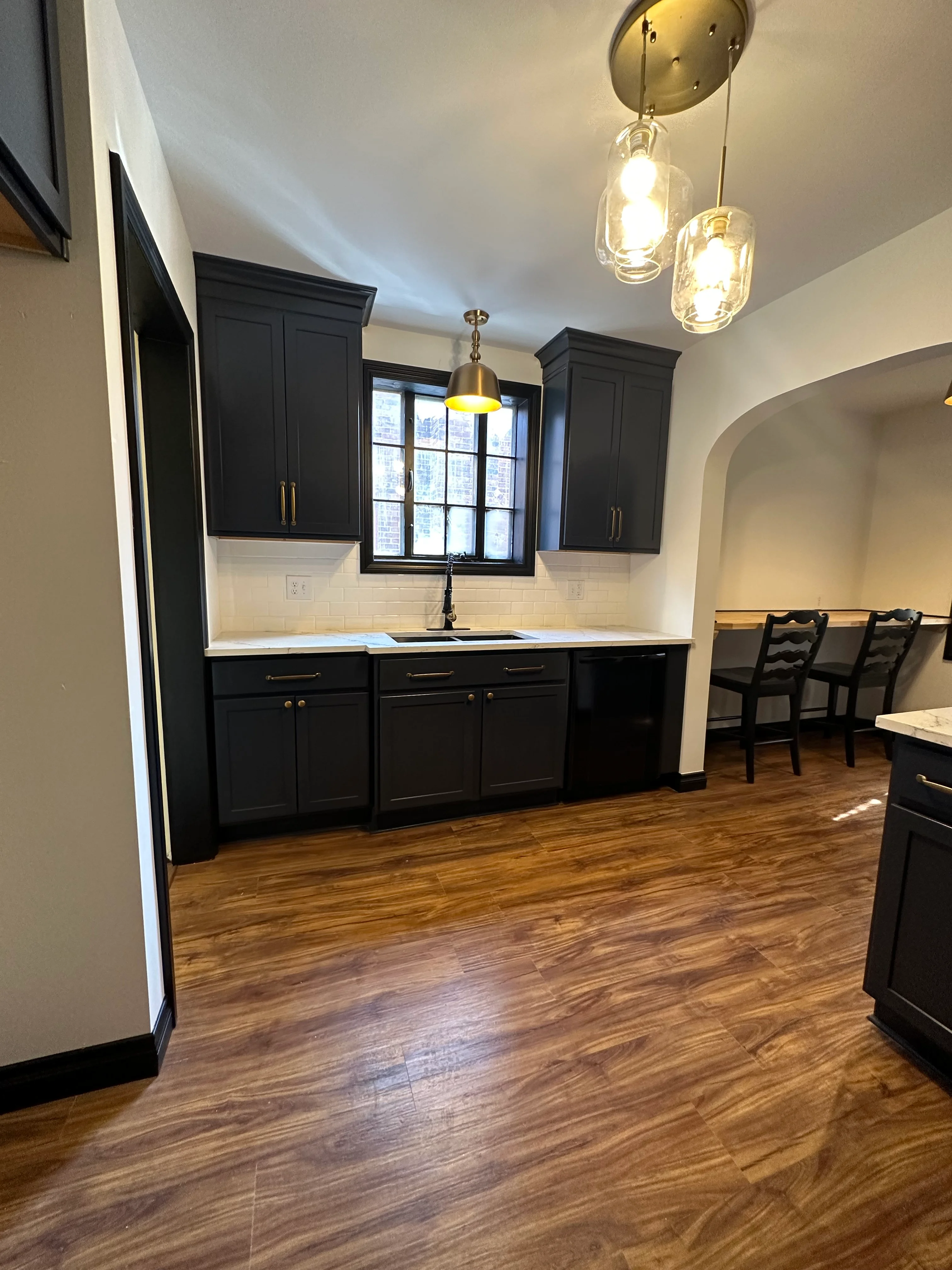 Black cabinetry kitchen with quartz counters, subway tile, and brass pendant lights
