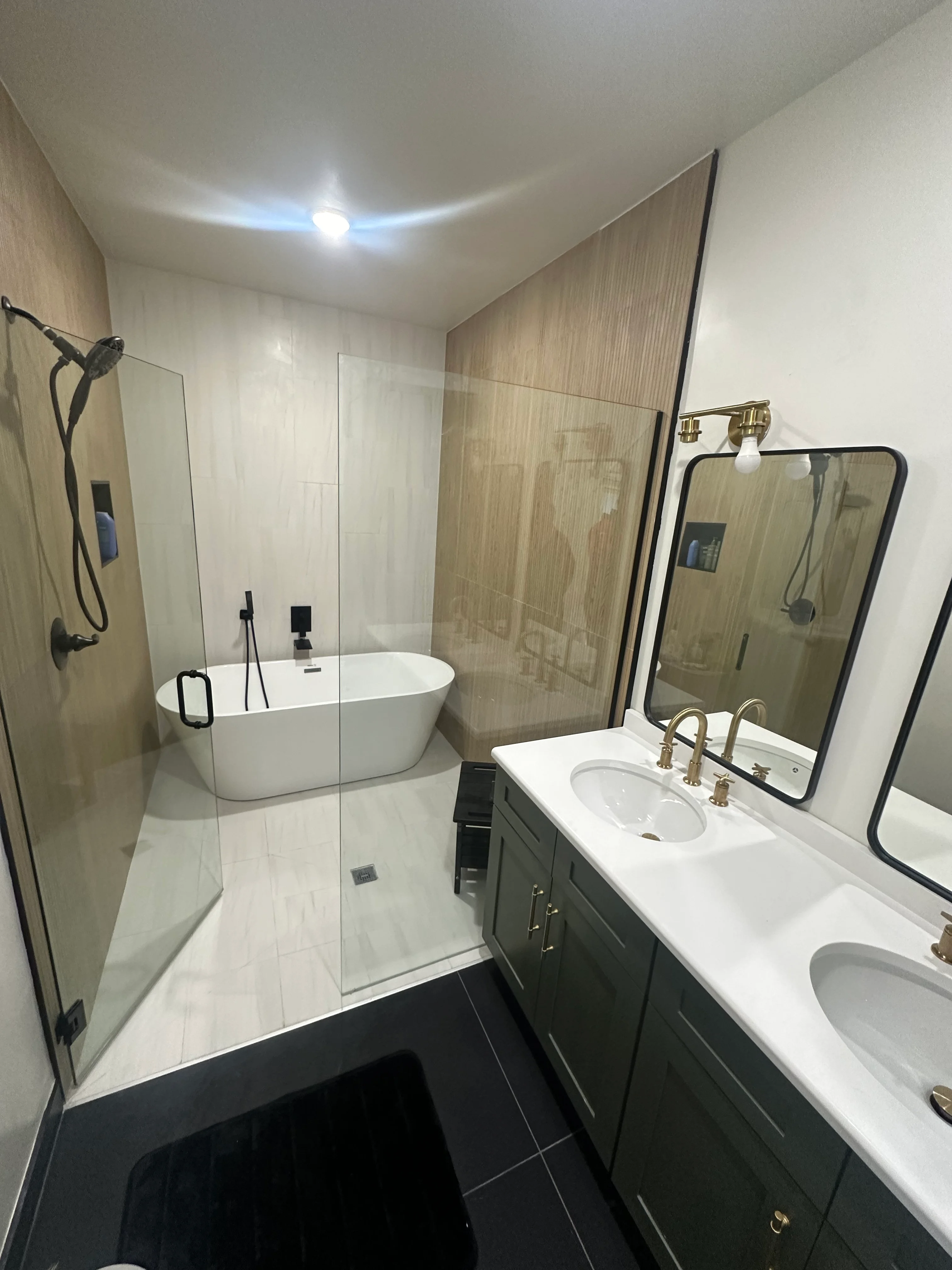 Modern bathroom with freestanding tub, dual vanity, frameless shower, and black tile flooring