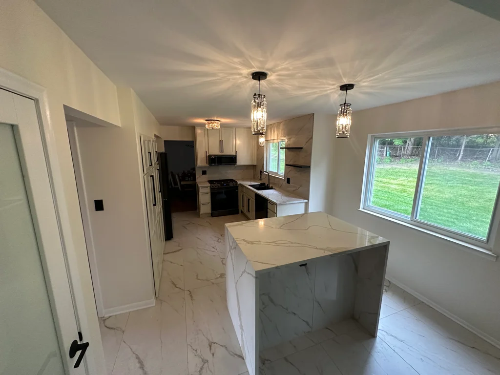 Modern kitchen with marble quartz island, white cabinets, black range, pendant lighting, and large windows