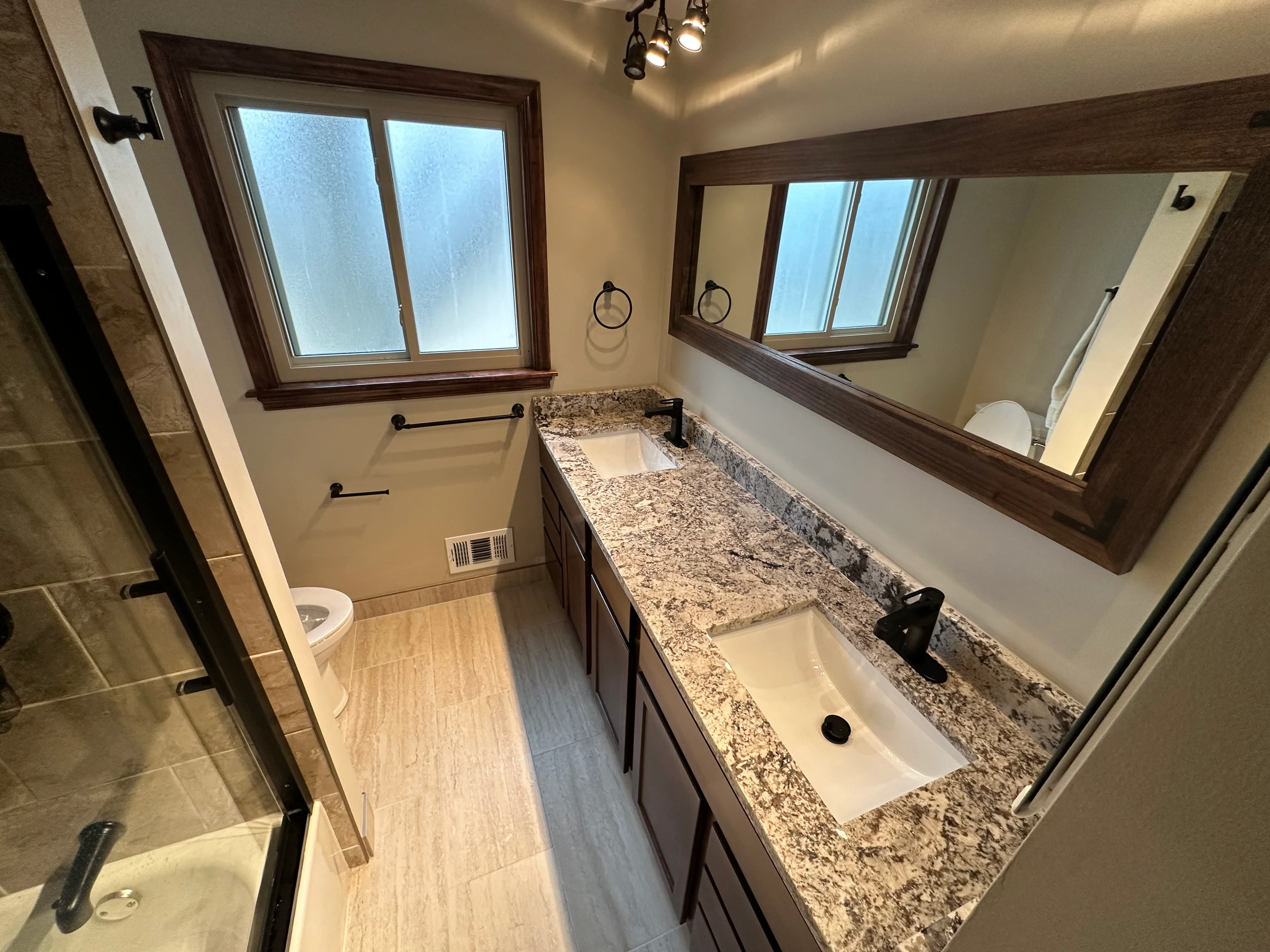 Dual-sink bathroom vanity with granite countertops, dark wood framing, and matte black fixtures