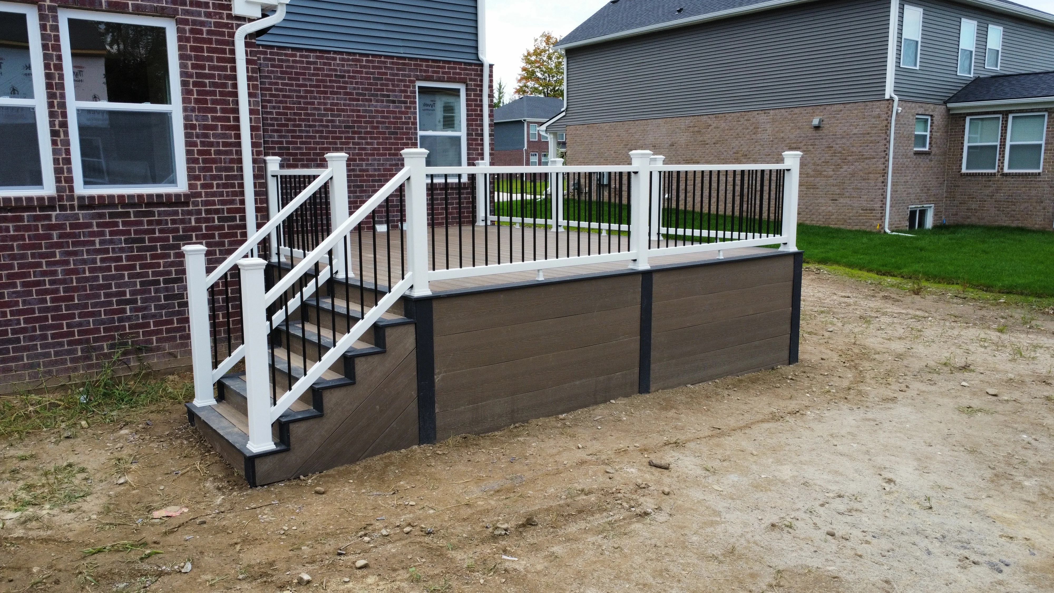 Elevated composite deck with white posts, black metal railing, and multi-step entry against brick home