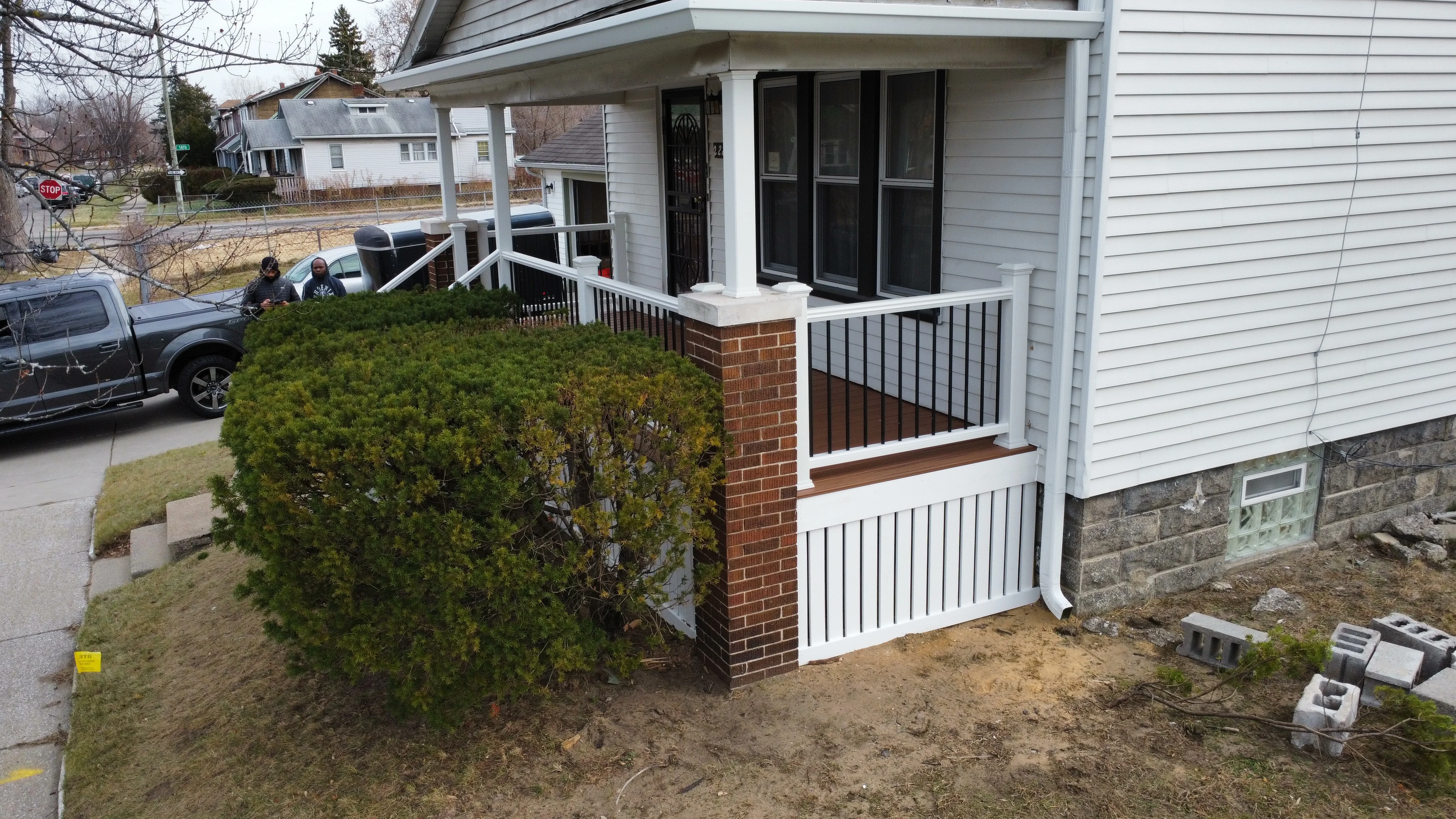 White composite deck porch with black metal railings and brick foundation base